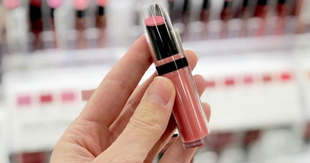 woman's hand holding lipstick at store in front of lipstick display