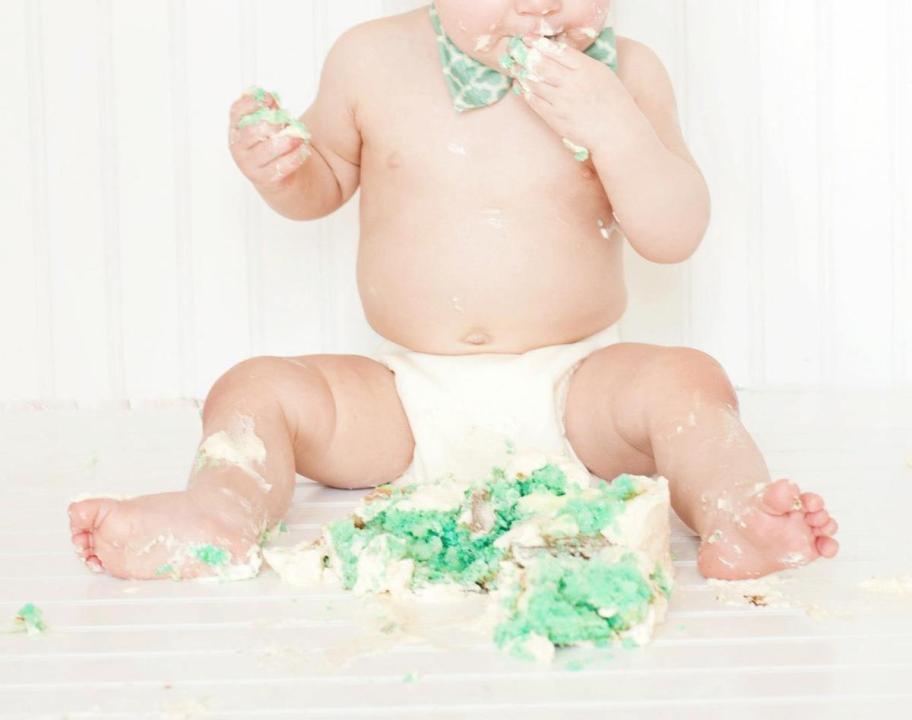 baby wearing cloth diaper eating blue cake on floor