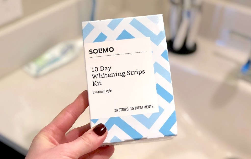 hand holding a box of Solimo Amazon teeth whitening strips in bathroom