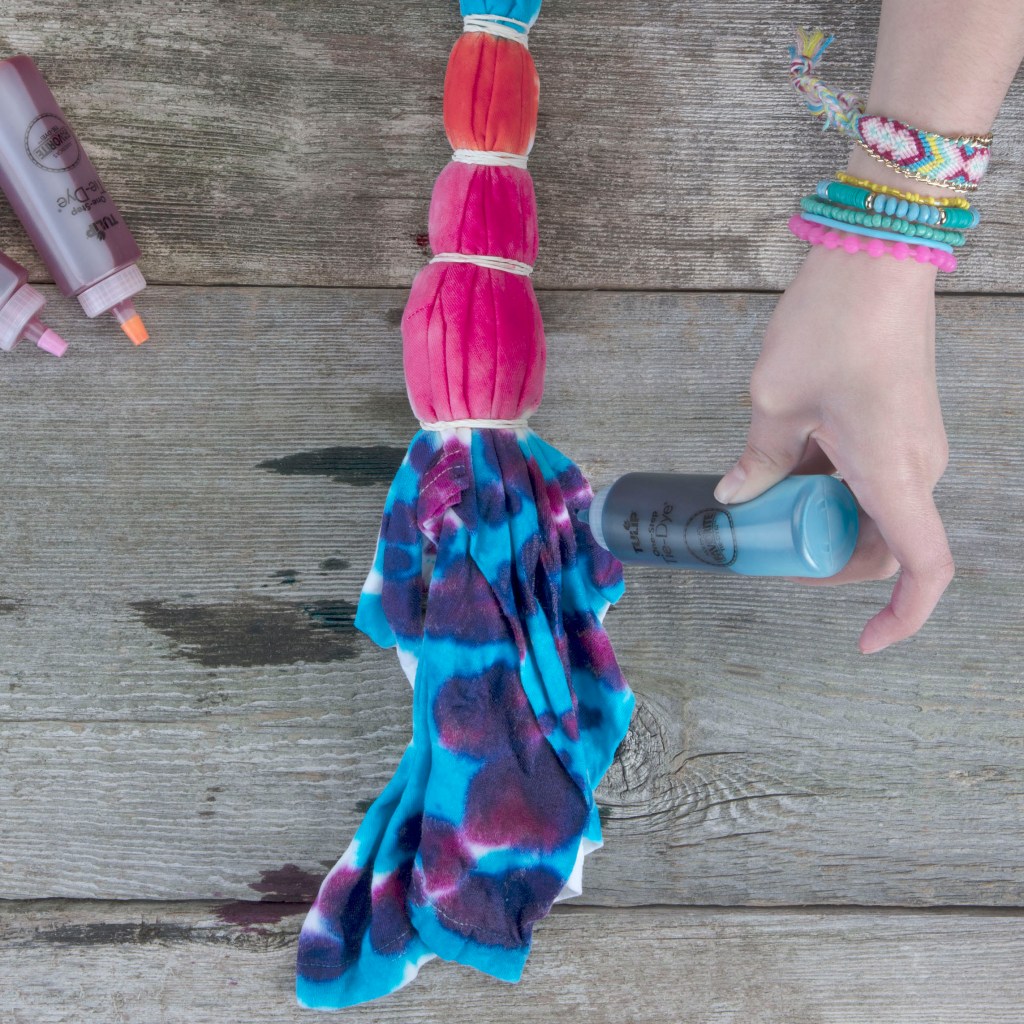 girls hand holding plastic squeeze bottle putting dye onto banded t-shirt for tie dye shirt project 