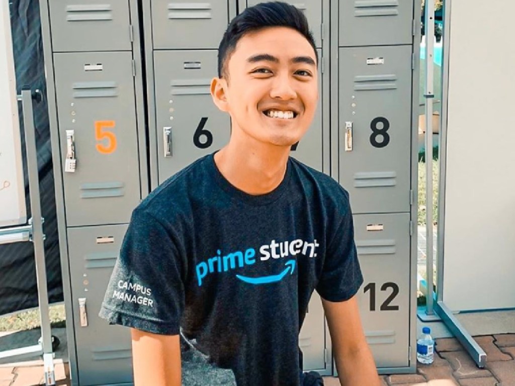 man sitting on a bench in front of lockers wearing prime student tee