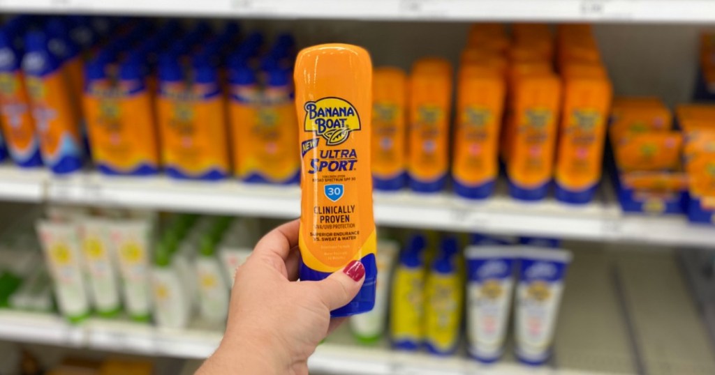 Woman's hand holding a bottle of sun screen in front of an in-store display