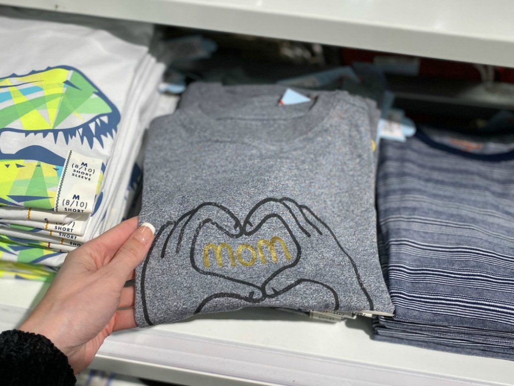 Woman holding a folded boys graphic tee that says 