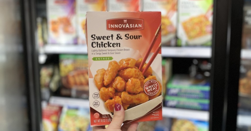 hand holding frozen asian chicken meal in front of store freezer