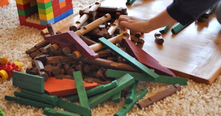 Child grabbing Lincoln Logs from pile on the floor 