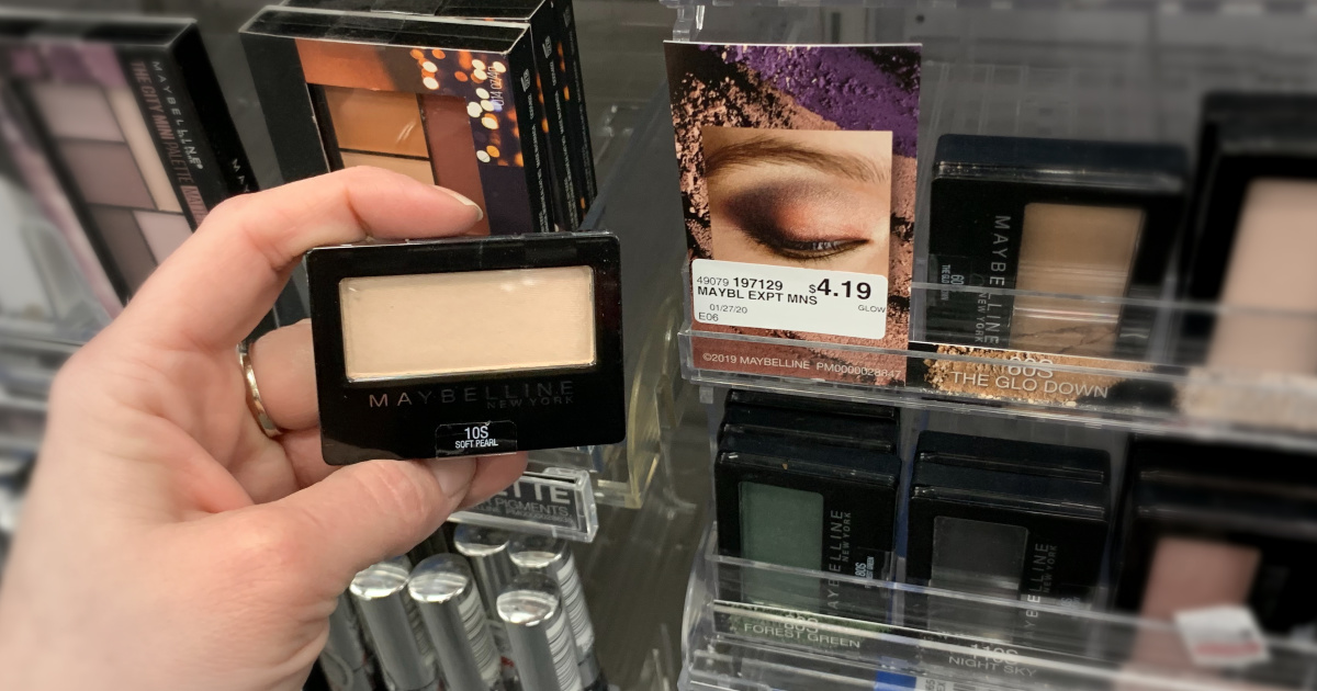 Hand holding eye shadow in front of shelf