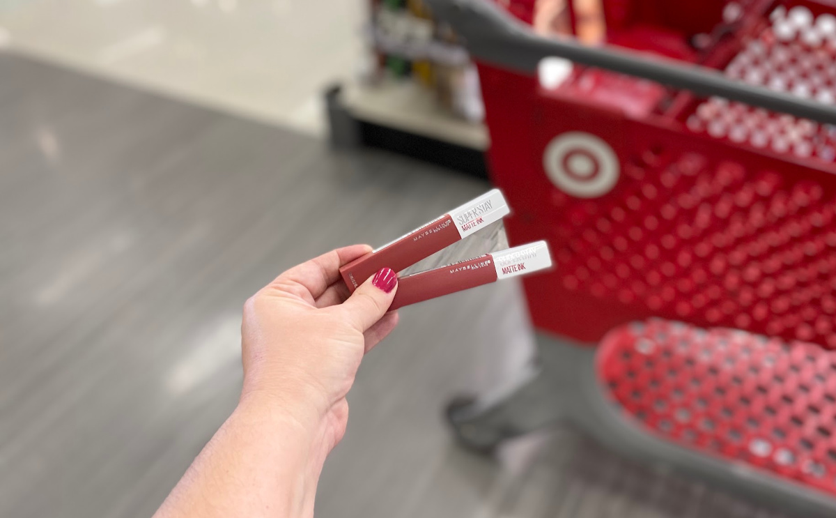 woman holding maybelline lipstick in front of Target cart