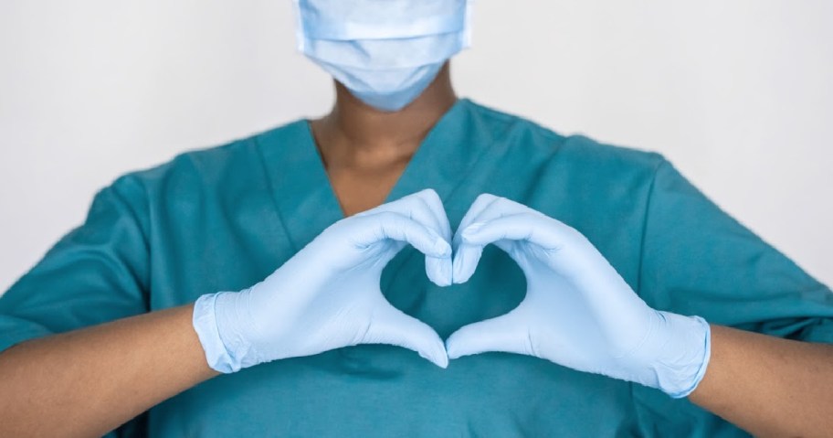 person in scrubs and gloves making a heart hand