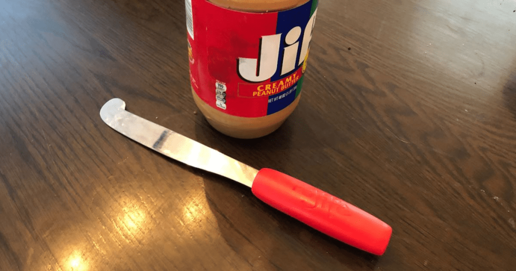 long red peanut butter spreader laying on counter with jar of jif peanut butter