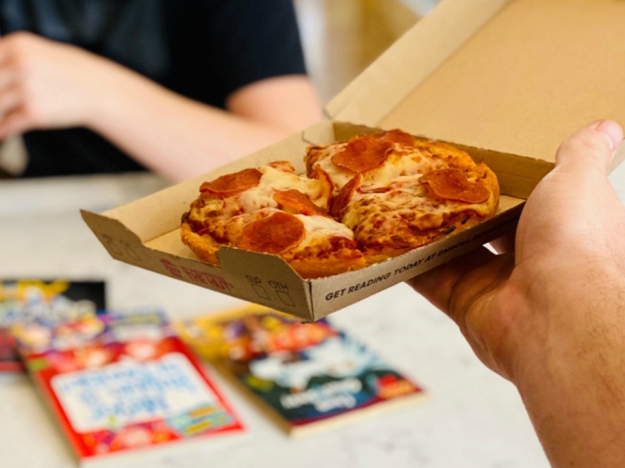 hand holding a personal pepperoni pizza in a box