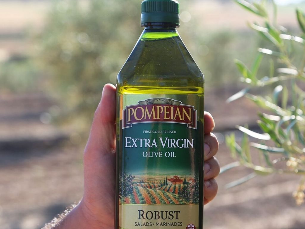 man's hand holding large bottle of olive oil in a field