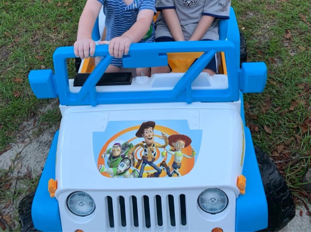 two kids inside Toy Story ride-on jeep toy outside