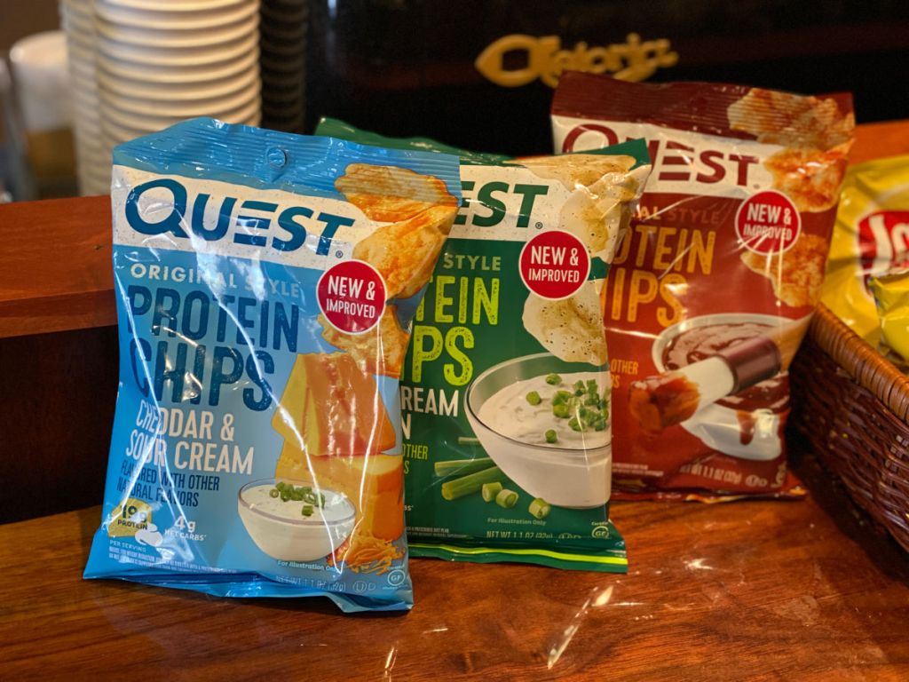 Quest Protein Chips cheddar and sour cream, bbq, and sour cream and onion bags all stacked together