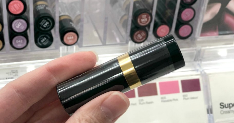 Hand holding tube of lipstick near in-store display