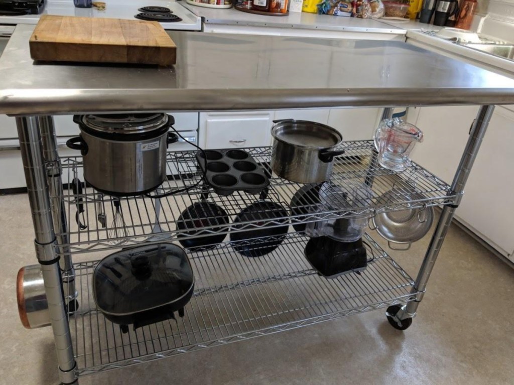 stainless steel work table in kitchen, with pots and pans on shelves