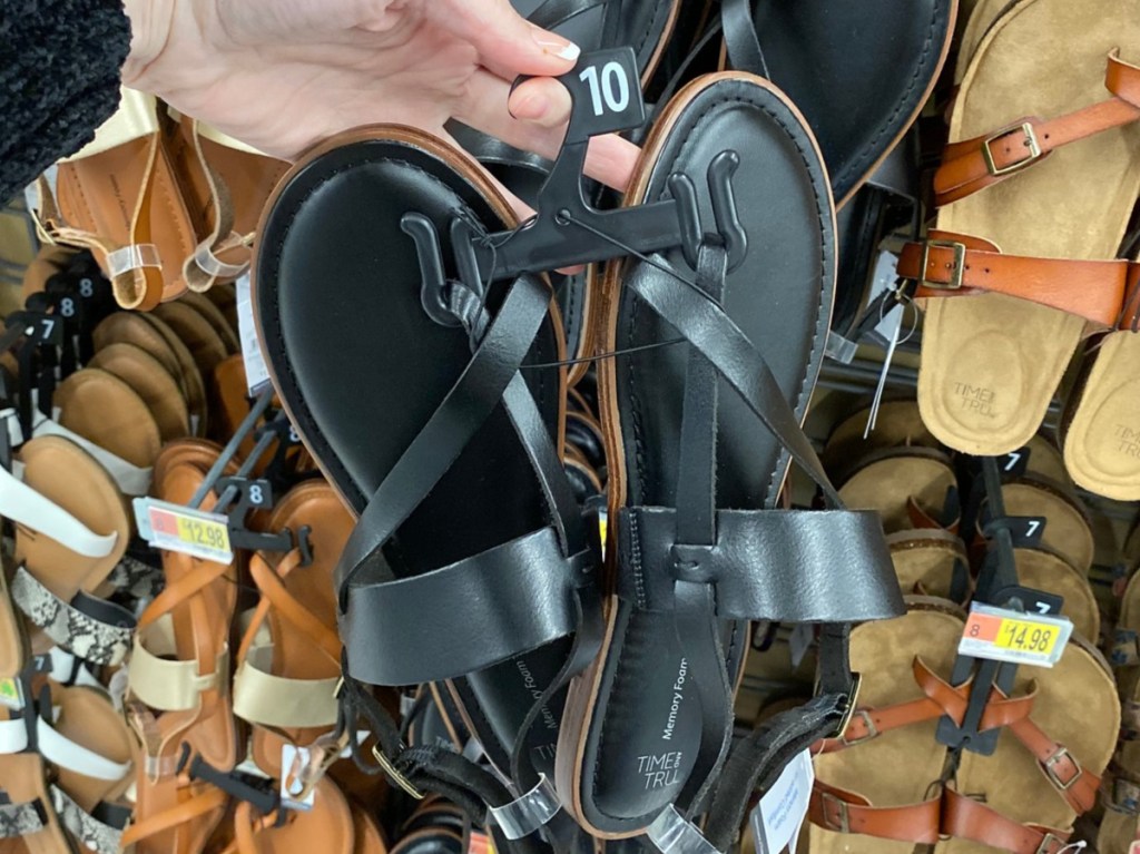 manicured hand holding black women's sandals in store aisle