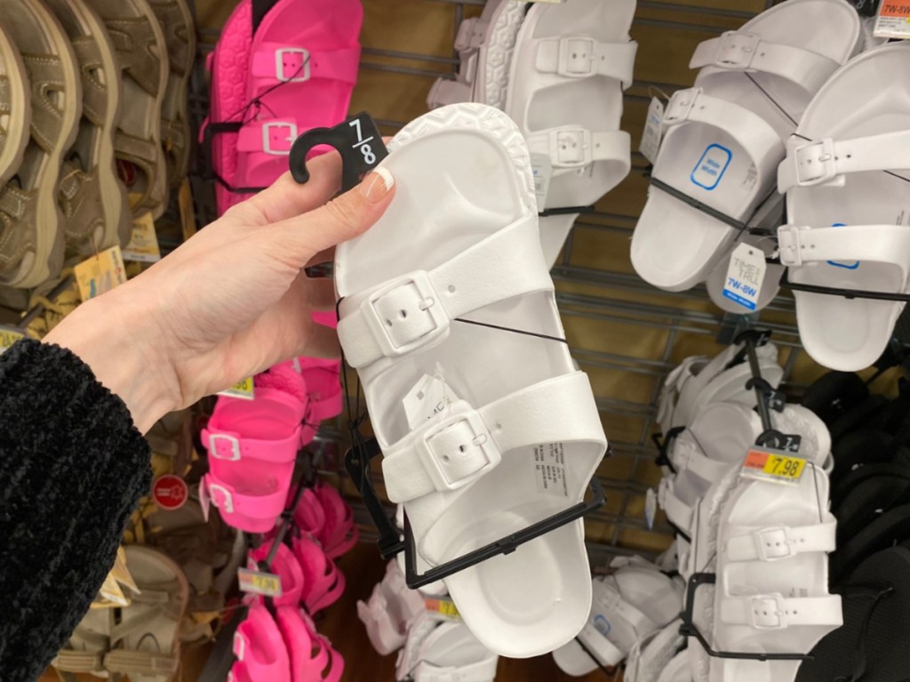 manicured hand holding white slide sandals in store aisle