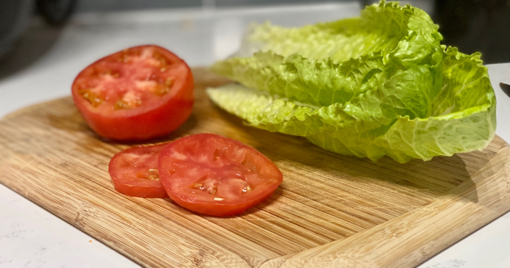 Lettuce and sliced tomatoes on a cutting board with knife
