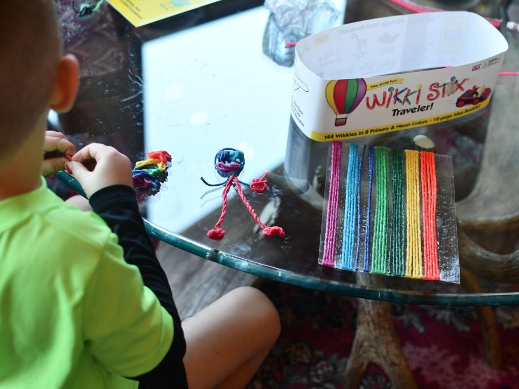 child with back turned playing with moldable wax covered yarn strips on table