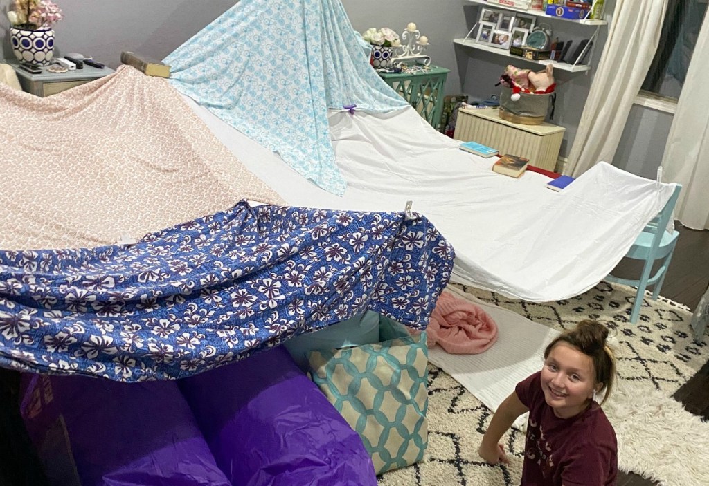 large indoor fort with blanket and girl smiling at camera