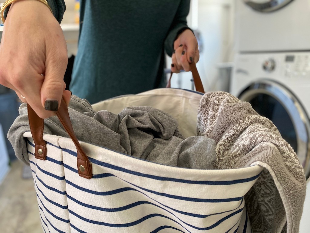 woman holding striped hamper filled with sheets and towels 