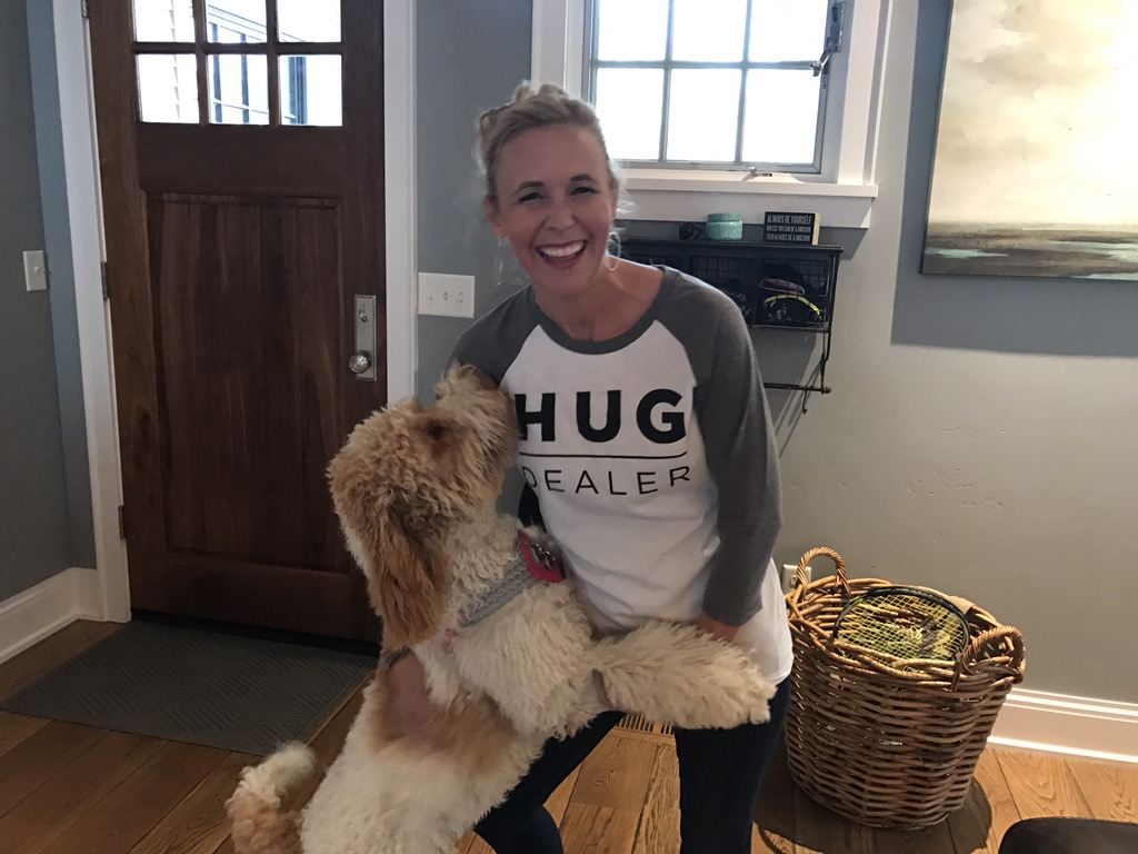 woman wearing hug dealer shirt with dog jumping up on her