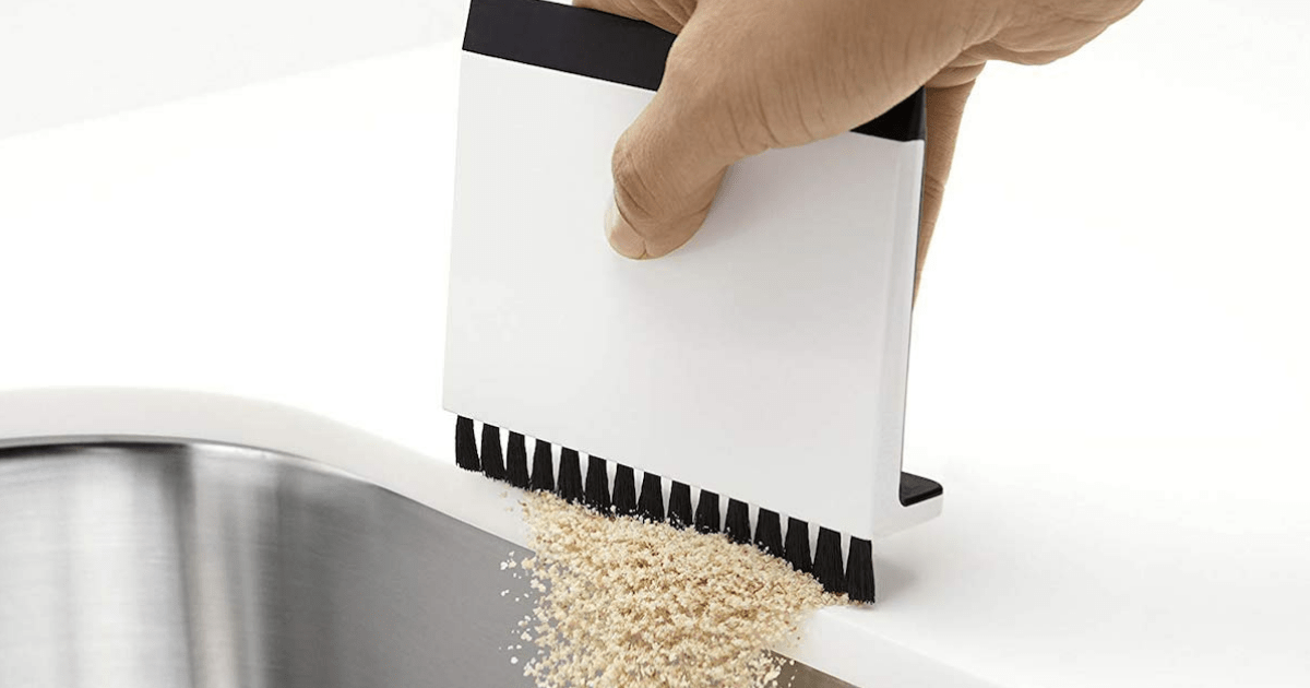 hand brushing crumbs off white countertop into sink