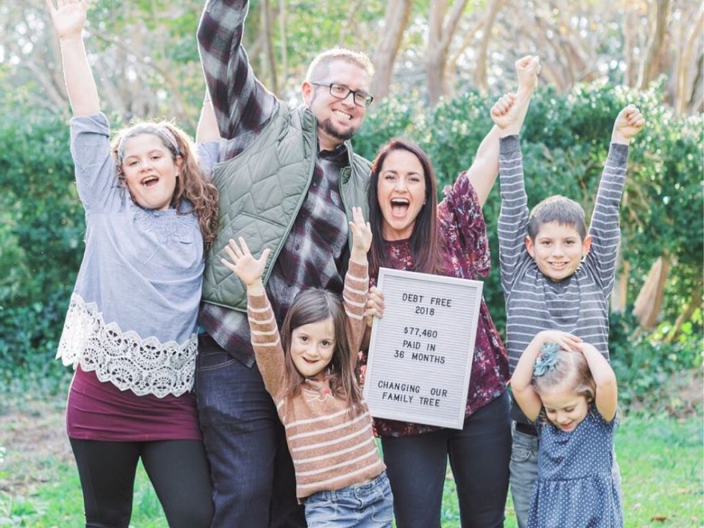 family holding up debt free sign and jumping with hands in the air