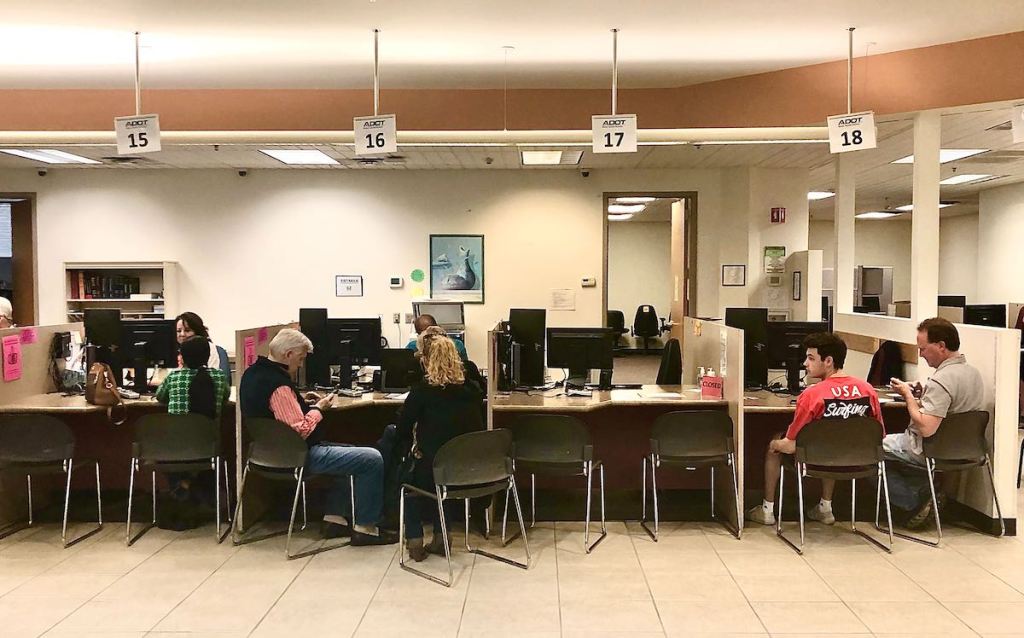 people sitting in chairs at the dmv at desks 