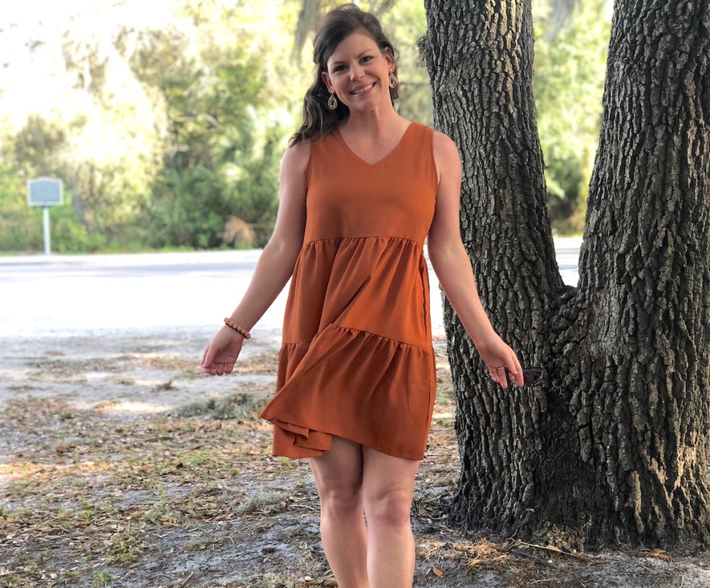 woman wearing orange strapless amazon spring dress smiling in front of large tree