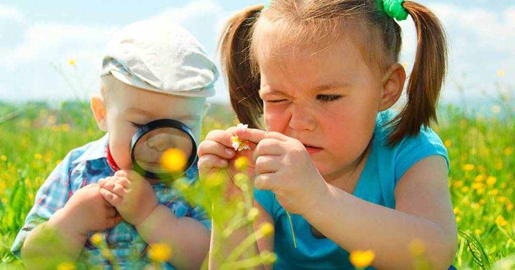 a little boy and a little girl playing in a field outside with a magnifying glass