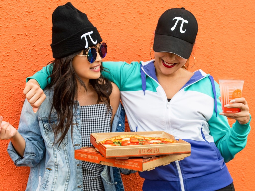 two women wearing Pi hats and holding pizza