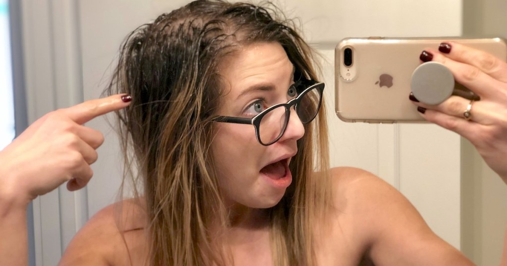woman pointing to greasy hair roots holding phone in mirror