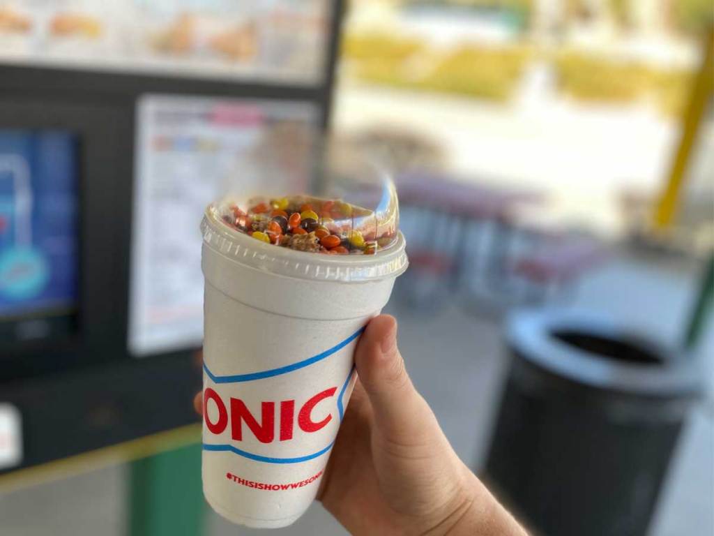 hand holding a cup of a shake with candy on top
