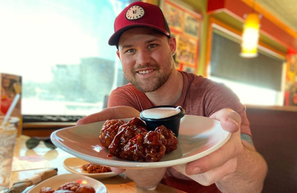 man holding a plate of boneless wings in a restaurant