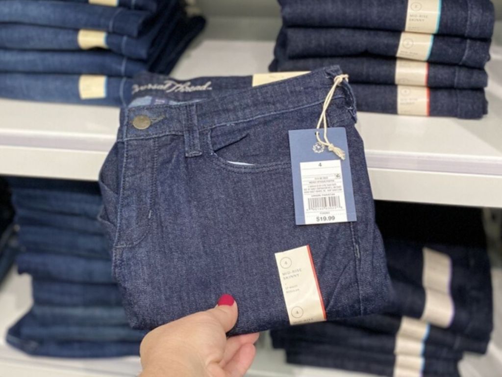 woman's hand holding pair of womens jeans folded at store