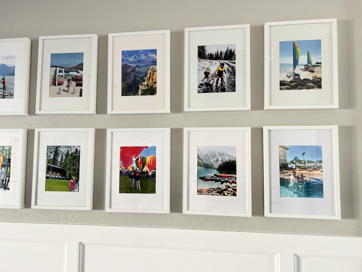 Gallery wall of white photo frames with personal travel photos. 