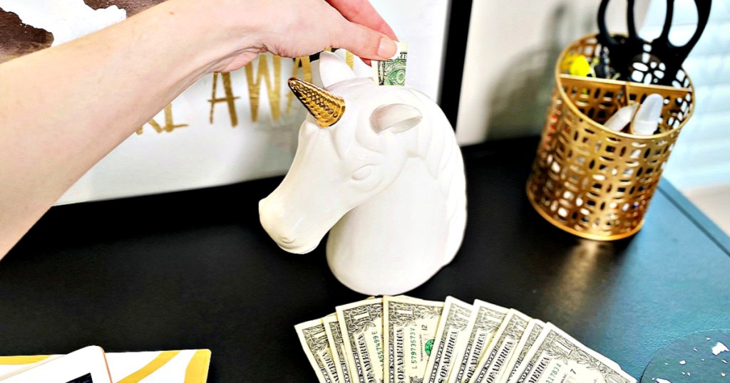 woman putting dollar bills in unicorn piggy bank