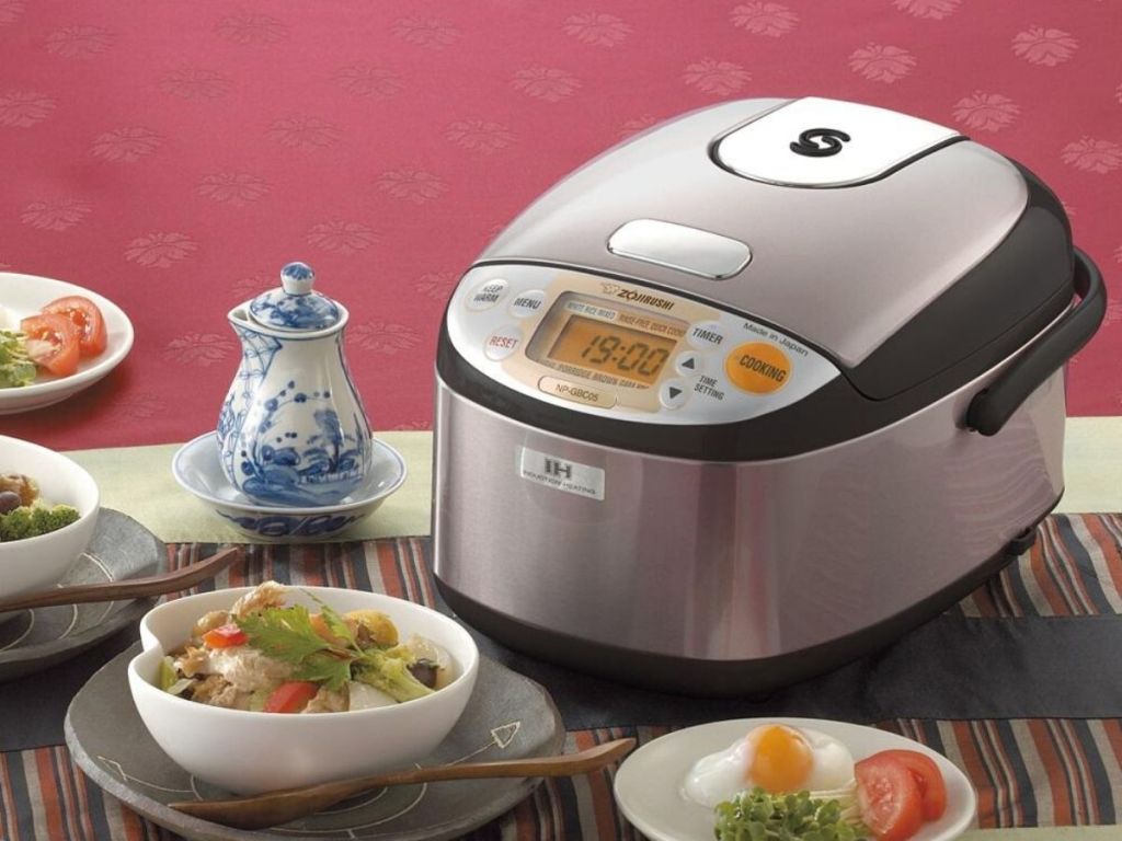 table with induction rice cooker and bowls of rice with asian food and soy sauce in pourer
