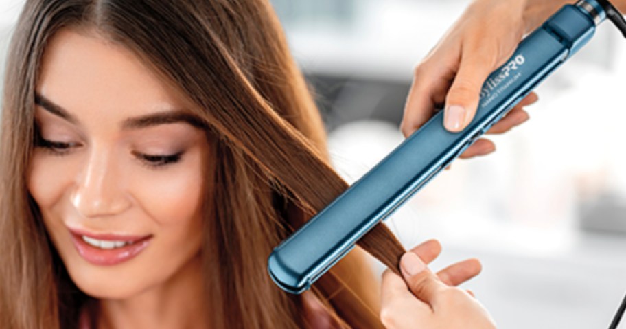 Woman sitting having her hair straightened with a blue flat iron