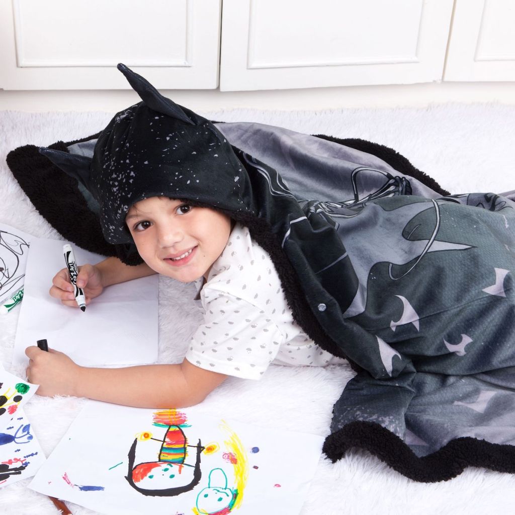 boy wearing Batman Snuggle Wrap Hoodie Blanket laying on the floor coloring with markers