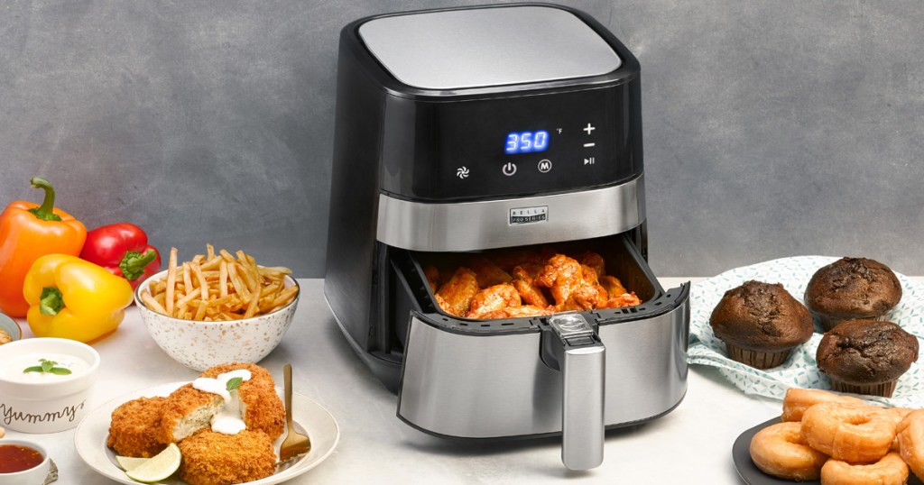 stainless steel and black air fryer with chicken wings in basket, and fried foods all around it