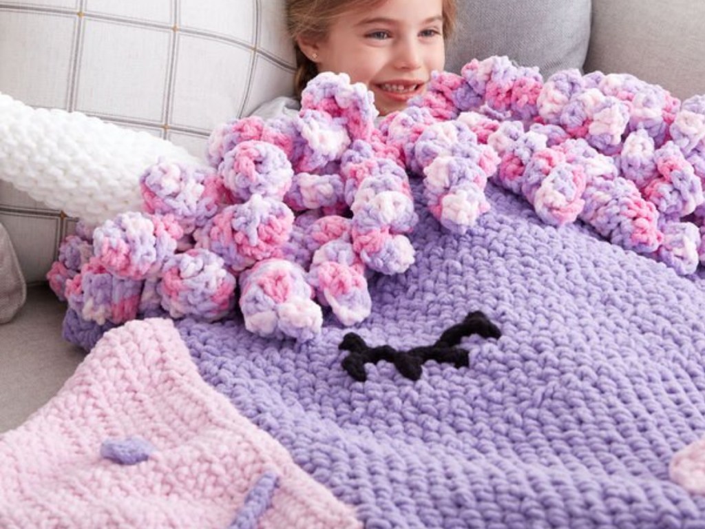 Little girl laying under a knitted unicorn blanket