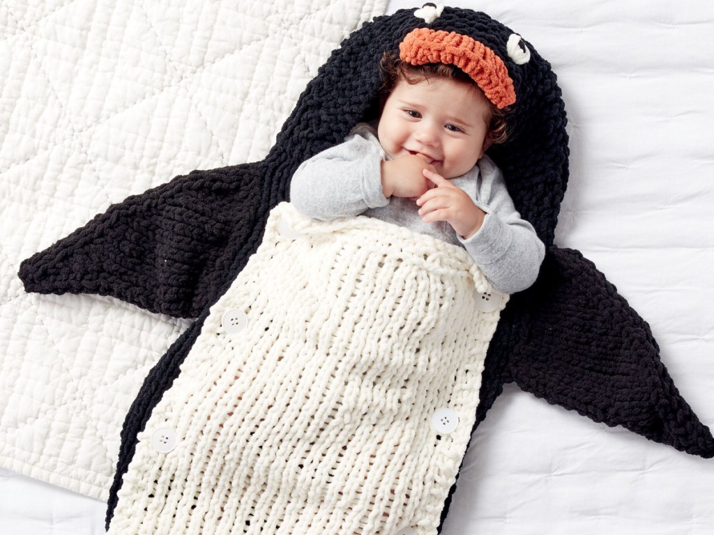 Bsby boy laying inside a knitted penguin blanket