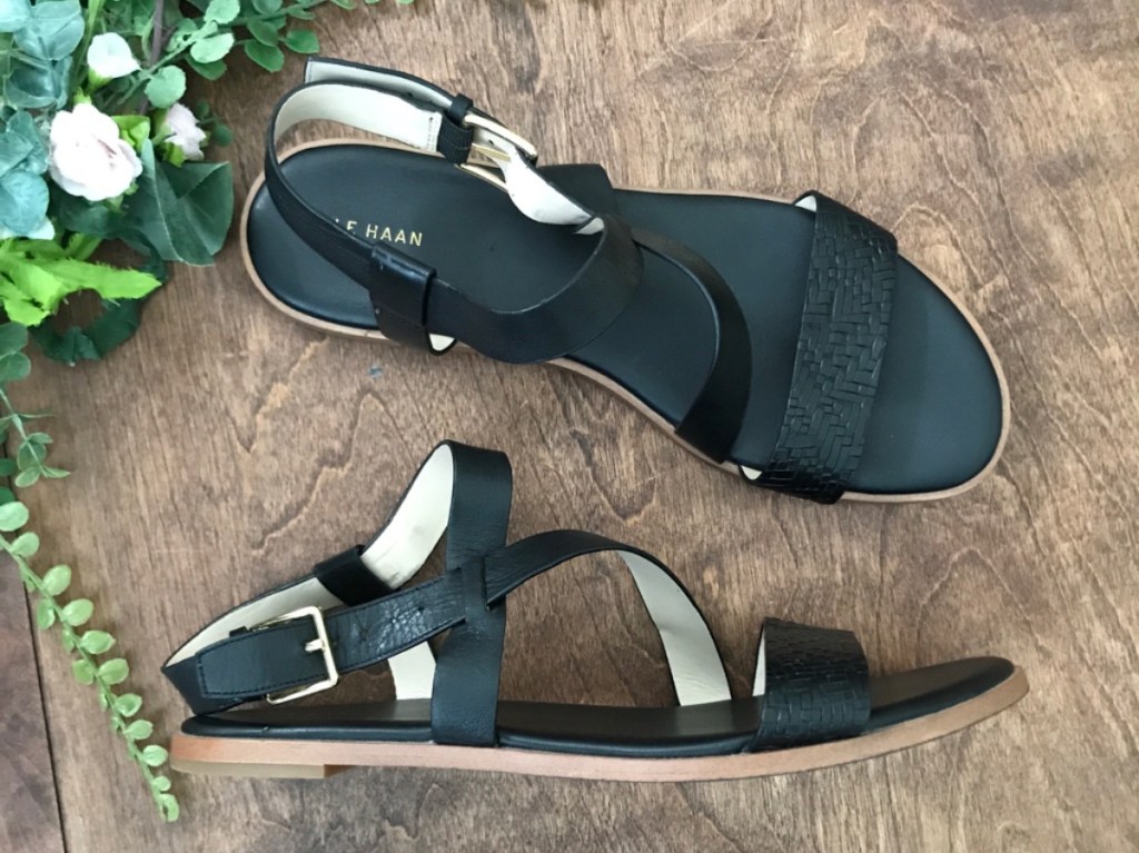 women's black strappy sandals on wood floor and plants