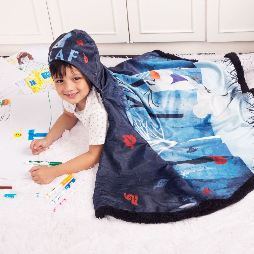 boy wearing Disney's Frozen 2 Olaf Snuggle Wrap Hoodie Blanket laying on the floor coloring