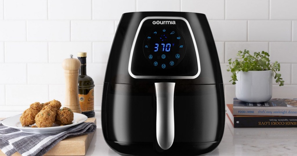 black air fryer with digital display sitting on kitchen counter next to fried chicken legs