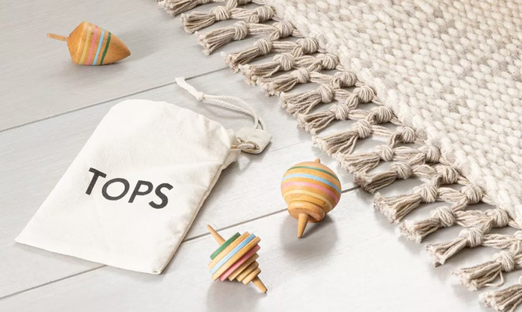 three wooden striped spinning tops laying on floor with white drawstring bag labeled tops