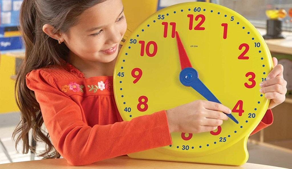 girl playing with large yellow plastic clock with red numbers and red & bluehands
