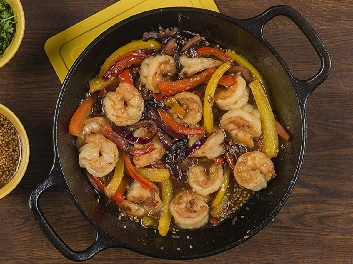 shrimp and veggies in black cast iron pan on wood table with bowls of seasoning